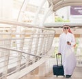 Arab man in travel concept . Young saudi arabic man in traditional clothes walking with suitcase on airport background.