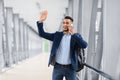 Arab Man Waving Hand And Talking On Cellphone While Walking In Airport Royalty Free Stock Photo