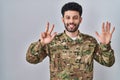 Arab man wearing camouflage army uniform showing and pointing up with fingers number eight while smiling confident and happy