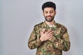 Arab man wearing camouflage army uniform smiling with hands on chest with closed eyes and grateful gesture on face