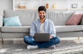 Arab millennial man using laptop computer, browsing internet, working online while sitting on floor at home Royalty Free Stock Photo