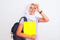 Arab student girl wearing hijab and backpack holding book over isolated white background with happy face smiling doing ok sign Royalty Free Stock Photo