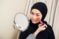 Arab woman applying makeup on her face, wearing traditional Arabian dress