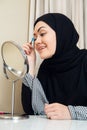 Arab woman applying makeup on her face, wearing traditional Arabian dress