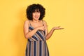Arab woman with curly hair wearing striped colorful dress over isolated yellow background amazed and smiling to the camera while Royalty Free Stock Photo