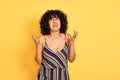 Arab woman with curly hair wearing striped colorful dress over isolated yellow background crazy and mad shouting and yelling with Royalty Free Stock Photo