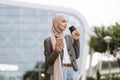 Arab woman in headscarf walking on the street with take away coffee and phone