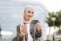 Arab woman in headscarf walking on the street with take away coffee and phone