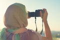 Arab Woman Photographer in a scarf taking picture using Camera on the sunset background. Halal travel concept Royalty Free Stock Photo