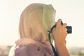 Arab Woman Photographer in a scarf taking picture using Camera on the sunset background. Halal travel concept Royalty Free Stock Photo