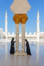 2 Arab women wearing traditional black burka clothing while praying in Sheikh Zayed Mosque in Abu Dhabi