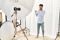 Arab young man posing as model at photography studio asking to be quiet with finger on lips pointing with hand to the side