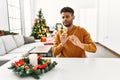 Arab young man sitting on the table by christmas tree disgusted expression, displeased and fearful doing disgust face because Royalty Free Stock Photo