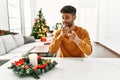 Arab young man sitting on the table by christmas tree pointing fingers to camera with happy and funny face Royalty Free Stock Photo