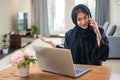 Arab young woman in abaya having conversation via mobile phone while sitting near laptop at her luxury accommodation Royalty Free Stock Photo