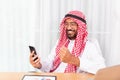 Arabian businessman happy reading a good news from his mobile phone in his office Royalty Free Stock Photo