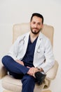 Arabian doctor surgeon in medical robe with phonendoscope seats in armchair in studio on white blanked background