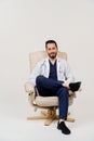 Arabian doctor surgeon in medical robe with stethoscope seats in armchair in studio on white blanked background