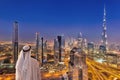 Arabian man watching night cityscape of Dubai with modern futuristic architecture in United Arab Emirates