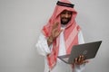 an arabian in a turban smiling and waving while using a laptop computer for an online meeting