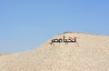 Arabic calligraphy text Tahya Misr (Long live Egypt) with the Egyptian flag on a hill with a blue sky