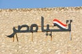 Arabic calligraphy text Tahya Misr (Long live Egypt) with the Egyptian flag on a hill with a blue sky