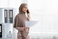 Arabic female manager talking on phone and holding papers in office Royalty Free Stock Photo
