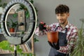 Arabic male gardener influencer films video for blog gives recommendations how to transplant potted flower, pouring