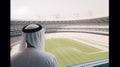 Arabic man looking out the window of a large modern football stadium