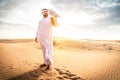 Arabic man with traditional emirates clothes walking in the desert with his falcon bird