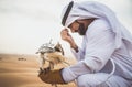 Arabic man with traditional emirates clothes walking in the desert with his falcon bird