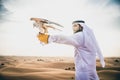 Arabic man with traditional emirates clothes walking in the desert with his falcon bird