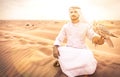 Arabic man with traditional emirates clothes walking in the desert with his falcon bird