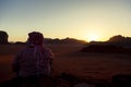 An arabic man wearing Jordanian keffiyeh head wrap is sitting on top of a rock overlooking the Wadi Rum Desert i Royalty Free Stock Photo