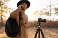 Arabic young photographer with backpack, camera and tripod surrounded by beautiful nature calling on mobile phone. Hiker