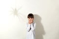 Arachnophobia. Scared little girl with dark hair and shadow of spider on wall, small kid looking directly at camera with big Royalty Free Stock Photo