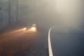 Dense mist forest road and car on the roadside with light beams
