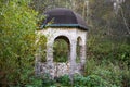 Arbor in the form of a small rotunda built from fragments of stone with arched windows in an overgrown area