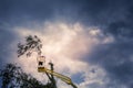 Unidentified arborist man in the air on yellow elevator, basket with controls, cutting off dead cherry tree Royalty Free Stock Photo