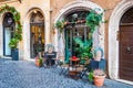 Arch door entrance of coffee bar called Caffe Novecento decorated with plants and flowers with standing tables and chairs. Cozy