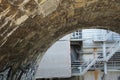 Arch made of stone cubes giving view to a back tract of an industrial buildings with pipes and metal staircase