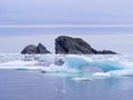 Arch shaped iceberg chunk with pair of rugged rock islets on the horizon in Twillingate Harbour