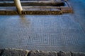 Archaeological remains of a Roman mosaic on the floor of a hallway with triangular figures and lines like blue and red labyrinths