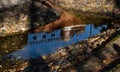 Arched bridge over a stream with a bright reflection of the sky with fallen autumn leaves