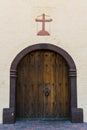 Arched rustic wood double doors under a cross in a plastered adobe wall of an old Spanish mission church Royalty Free Stock Photo