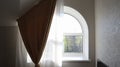 Arched window in the living room with tulle and curtain. Modern and bright bedroom interior.