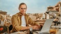 Archeological Digging Site: Portrait of Great Male Archaeologist Doing Research, Using Laptop, Looks