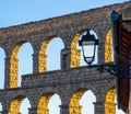 The arches of the Segovia aqueduct illuminated by the evening sunlight. The streetlights shine by the sun. Royalty Free Stock Photo
