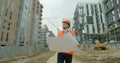 Architect or builder man walking on the construction site and analyzing scheme project plan. Young architect or builder