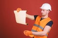 Architect concept. Man in helmet, hard hat holds building plan, controls works, red background. Engineer, architect Royalty Free Stock Photo